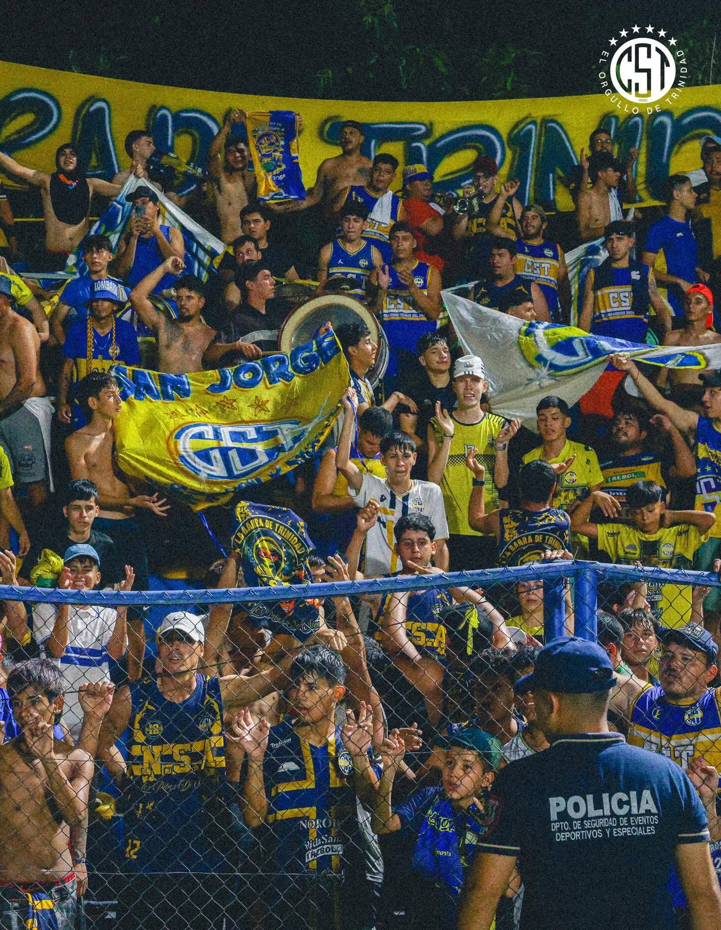 Hinchada de Trinidense con banderas azules y amarillas